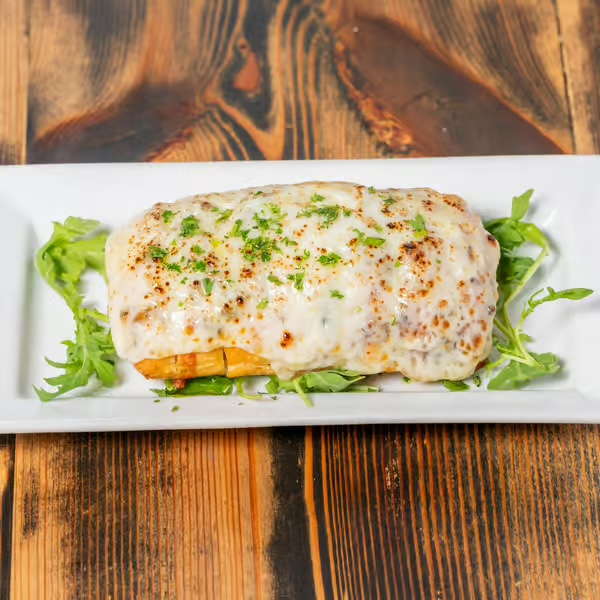 Cheesy baked plantain dish topped with parsley, served on a white plate with arugula.