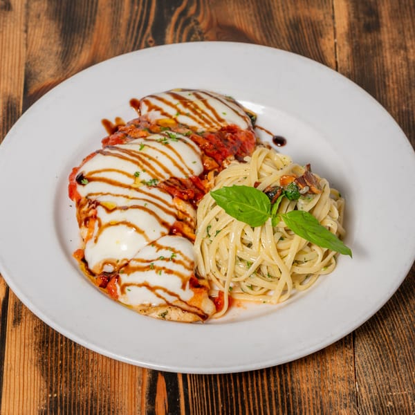 Chicken parmesan with melted mozzarella, tomato sauce, balsamic glaze, and a side of pasta.
