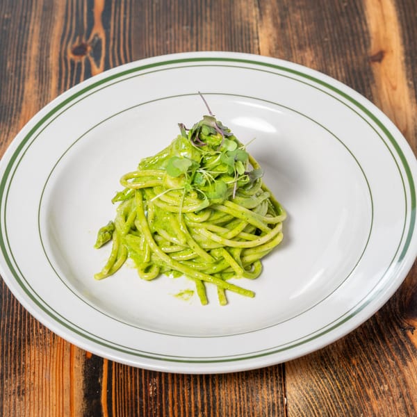 Green pesto pasta with microgreens on a white plate with green stripes, on a wooden table.