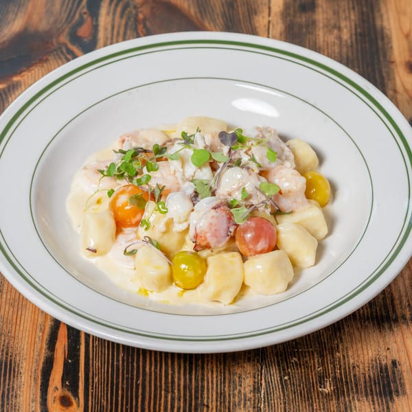 Lobster gnocchi with cherry tomatoes and microgreens in a creamy sauce on a white plate.