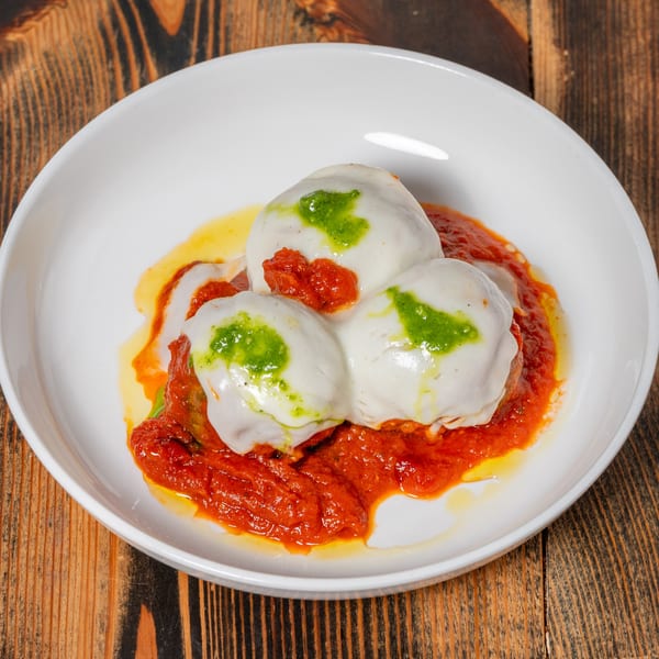 Three meatballs covered in melted mozzarella, red sauce, and green pesto in a white bowl.