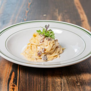 Creamy pasta with mushrooms and microgreens on a white plate with green trim, on a wooden table.